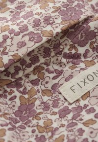 Blumenstoff in Creme mit kleinen lila und braunen Blumen und einer strukturierten Oberfläche. Enthält ein sichtbares Etikett mit "FIXON."