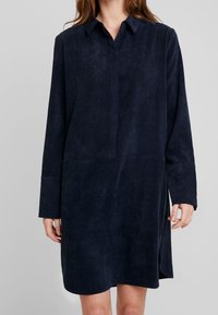 Mörkblå kordcostymklänning med krage, knapplist, långa ärmar och sidofickor. Mjuk textur med avslappnad passform.