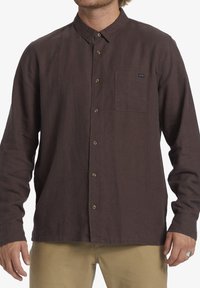 Brown button-up shirt made of lightweight fabric. Features a chest pocket, long sleeves, and a classic collar design with button-down front.