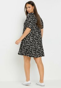 Musta kukkamekko, jossa on lyhyet hihat, kerrostettu vyötärö ja röyhelöinen helma; koristeltu pienillä valkoisilla ja vaaleanpunaisilla kukilla. Yhdistetty valkoisten tennareiden kanssa.