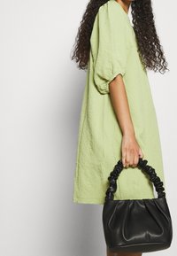 Robe texturée vert clair avec des manches bouffantes, accompagnée d'un petit sac à main en cuir noir avec une poignée tressée.