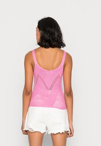 Top in maglia rosa a maniche larghe, con motivo a zigzag e design in maglia aperta, abbinato a pantaloni corti bianchi strappati.