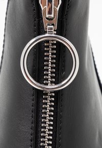 Black leather bag featuring a prominent silver zipper with a circular pull tab. The zipper is parallel to textured fabric accents.