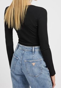 Zwarte ribbelige top met lange mouwen, gecombineerd met hoog opgesneden lichtblauwe spijkerbroek met een opvallende driehoekige leren patch op de achterzak.