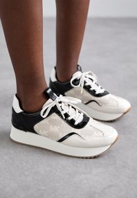 White and black sneakers with a textured upper featuring a repeating "MK" pattern, white laces, and rubber soles.