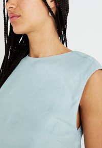 Blouse sans manches bleu clair à encolure ronde, fabriquée en tissu lisse. Présente des lignes épurées et des détails de couture minimalistes.