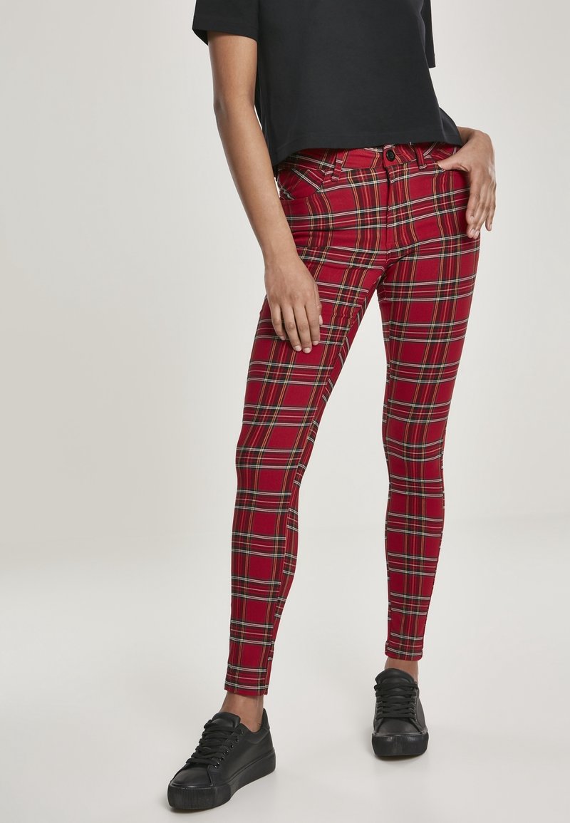 Jean skinny à carreaux rouges avec des accents noirs et jaunes, fabriqué en tissu stretch. Associé à un t-shirt noir court et des baskets noires.