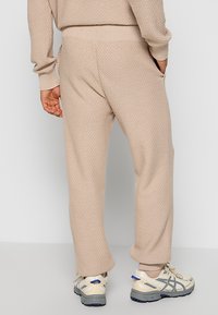 Beige knit sweatpants with textured fabric, relaxed fit, side pockets, and elastic waistband. Suitable for casual wear and comfort.