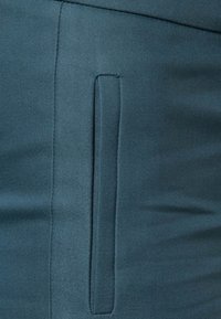 Close-up van teal stof met een gladde textuur en een verborgen zijzak, die een elegante, op maat gemaakte uitstraling toont.