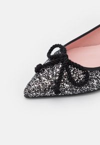 Svarta glittriga balettklackar med spetsig tå, med en svartsnoddad lace-dekoration och en mjuk rosa insida. Slät textur.