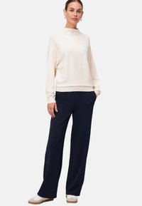 Pull crème à côtes avec un col montant associé à un pantalon large bleu marine. L'ensemble comprend des poches latérales et est complété par des baskets blanches.