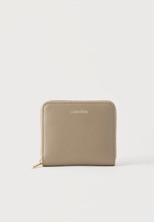 Μπεζ πορτοφόλι Calvin Klein με φερμουάρ που κλείνει γύρω, χρυσό φερμουάρ και λογότυπο σε λείο δερμάτινο φόντο, σε λευκό φόντο.