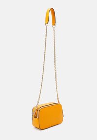 Bolso cruzado de cuero amarillo con cadena. Forma rectangular, cierre de cremallera y detalles en negro. Textura suave con acentos metálicos.