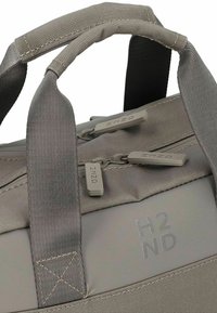 Sac gris texturé avec de courtes poignées, doté de deux zippers et de l'inscription en relief "H2ND". Fabriqué en tissu durable avec une finition mate.