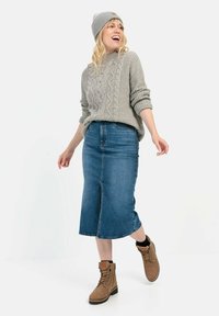 Grå kabelstrikket sweater, midilengde blå denimnederdel og tan snørebåndsstøvler. Modellen poserer mod en hvid baggrund.
