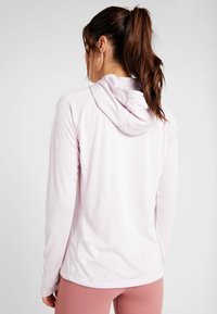 Helle rosa Kapuzenoberteil mit langen Ärmeln, glatter Textur, taillierter Passform und verstellbarem Kordelzug an der Kapuze. Weicher Stoff und nahtlose Schultern.