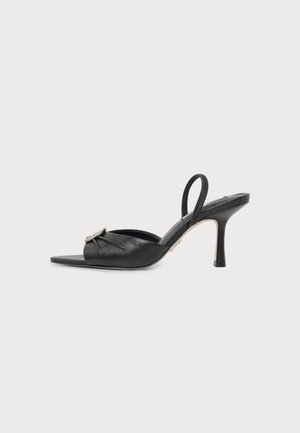 Zwarte leren open teen hoge hak mule met slingback bandje en zilveren gesp detail aan de voorkant tegen een egale achtergrond.