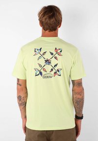 T-shirt vert clair à manches courtes avec un imprimé floral et géométrique coloré au dos, avec le texte "OXBOW" au centre.