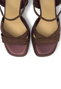 Sandales ouvertes pour femme avec lanières tressées marron et semelles carrées bordeaux sur fond blanc.