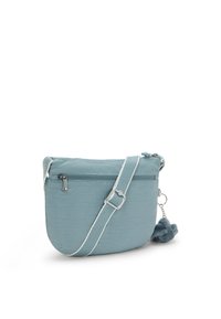 Ljusblå crossbody-väska gjord av texturerad tyg, med en zip-ficka, justerbar rem och en pom-pom charm fäst.