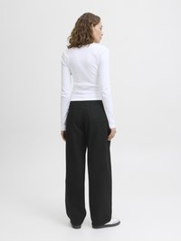 White ribbed long-sleeve shirt paired with loose-fitting, high-waisted black pants and white sneakers, viewed from the back.