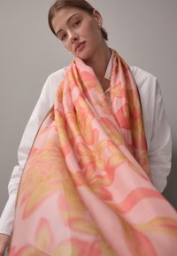 Kukkahuivi vaaleanpunaisena, jossa keltaisia korostuksia. Kevyt kangas laskeutuu tyylikkäästi. Suuret, tyylitellyt kukkakuviot koristavat huivia.