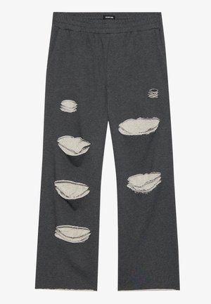 Dunkelgraue Hose mit mehreren großen abgenutzten und ausgefransten Patches, die einen helleren Stoff darunter freilegen.