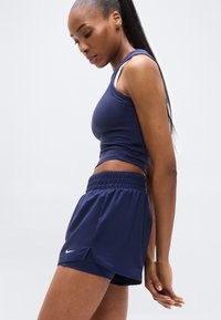 Marineblåt atletisk tanktop med tætsiddende pasform og tynde stropper, kombineret med matchende marineblå shorts med elastisk linning og sideslidser.