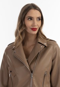 Giacca moto in ecopelle marrone con chiusura a zip, hardware argentato e colletto inclinato. Presenta una tasca sul petto e tasche laterali con zip.