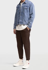 Veste en denim bleu clair, pantalon marron et baskets montantes blanches avec un accent en forme de cœur. Comprend des poches et une coupe décontractée.