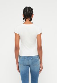 Tricou alb cu maneci scurte, cu guler rotund, asortat cu jeansi din denim bleu deschis, care au buzunare la spate cu cusături subtile.