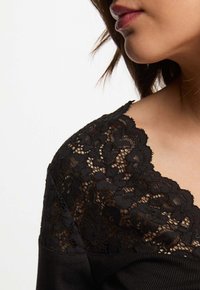 Zwarte top met kantdetails op de halslijn, met een gladde textuur en een aansluitend ontwerp. Het kant heeft een bloemmotief.