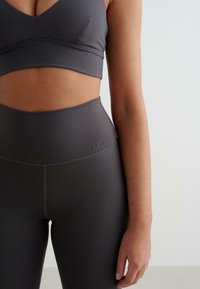 Grijze sportbeha en high-waisted leggings van glad materiaal, met minimale branding en een naadloos ontwerp.