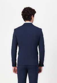 Marineblaues Sakko mit taillierter Passform, schmalen Revers und einer Mittelschlitz hinten. Der Stoff wirkt glatt mit subtiler Textur.