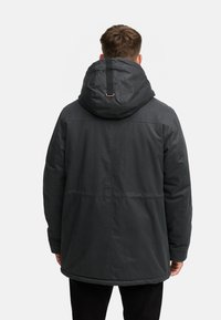 Donkergrijze pufferjas met een grote kap, horizontale stiksels en elastische manchetten. Het materiaal lijkt glad en licht glanzend.