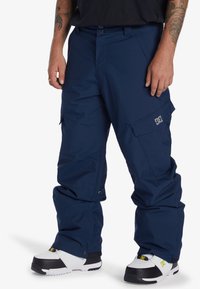 Mörkblå vattentäta snöbyxor med avslappnad passform, fickor i cargostil och logodetalj. Tillverkade av slitstarkt material med justerbara ärmslut.