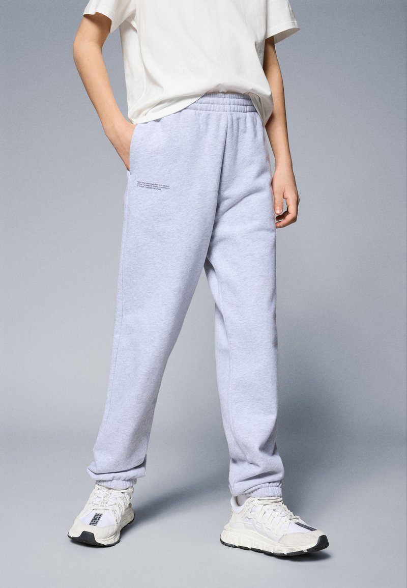 Pantalones de chándal grises con cintura elástica y bolsillos laterales. Combinados con zapatillas blancas con detalles en negro. Diseño simple y de corte relajado.