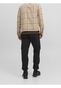 Beige kostkovaná overshirt v kombinaci s černými cargo kalhotami s bočními kapsami, elastickými manžetami a černými teniskami. Jednoduchý, funkční design.