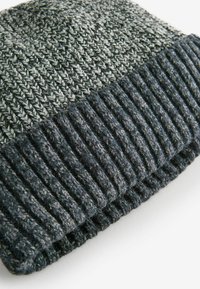 Mörkt grå stickad mössa med en trendig textur på toppen och ribbat underavsnitt. Tillverkad av en ullblandning för värme, med en blandning av ljusa och mörka fibrer.