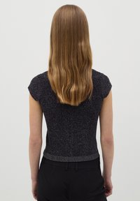 Top negro ajustado de manga corta con detalles de hilo metálico y textura acanalada, diseño corto, combinado con pantalones de talle alto.