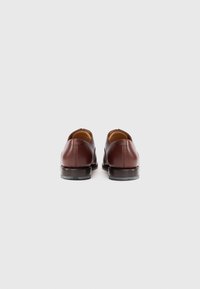 Un par de zapatos de vestir de cuero marrón vistos desde atrás sobre un fondo blanco liso.