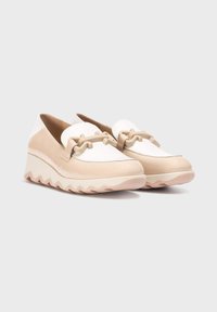 Zapatillas beige y blancas sin cordones con parte superior de cuero texturizado, una correa decorativa y suela gruesa con zigzag. Acabado suave y puntera redondeada.
