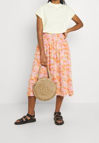 Ljusgul kortärmad t-shirt i kombination med en rosa blommig midikjol. Håller en rund vävd stråväska. Svarta sandaler med remmar.