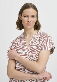 Krátký rukáv v béžové barvě s pruhy v rezavé barvě zebra, s výstřihem do V a volným střihem, vyrobený z lehké texturované látky.