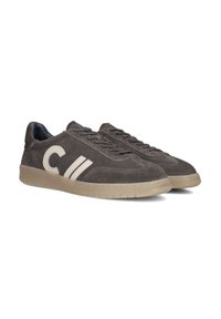 Gray suede sneakers feature a rounded toe, side logo, and contrasting beige accents. The rubber sole has a textured grip pattern.