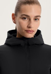 Černá kapucňová bunda vyrobená z hladkého materiálu, s plným zipem a těsnou kapucí. Čisté linie a minimalistický design.