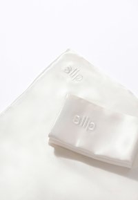 Silkepose og matchende scrunchie i off-white med brodert logo. Glatt tekstur med blank overflate. Rektangulære og ovale former.