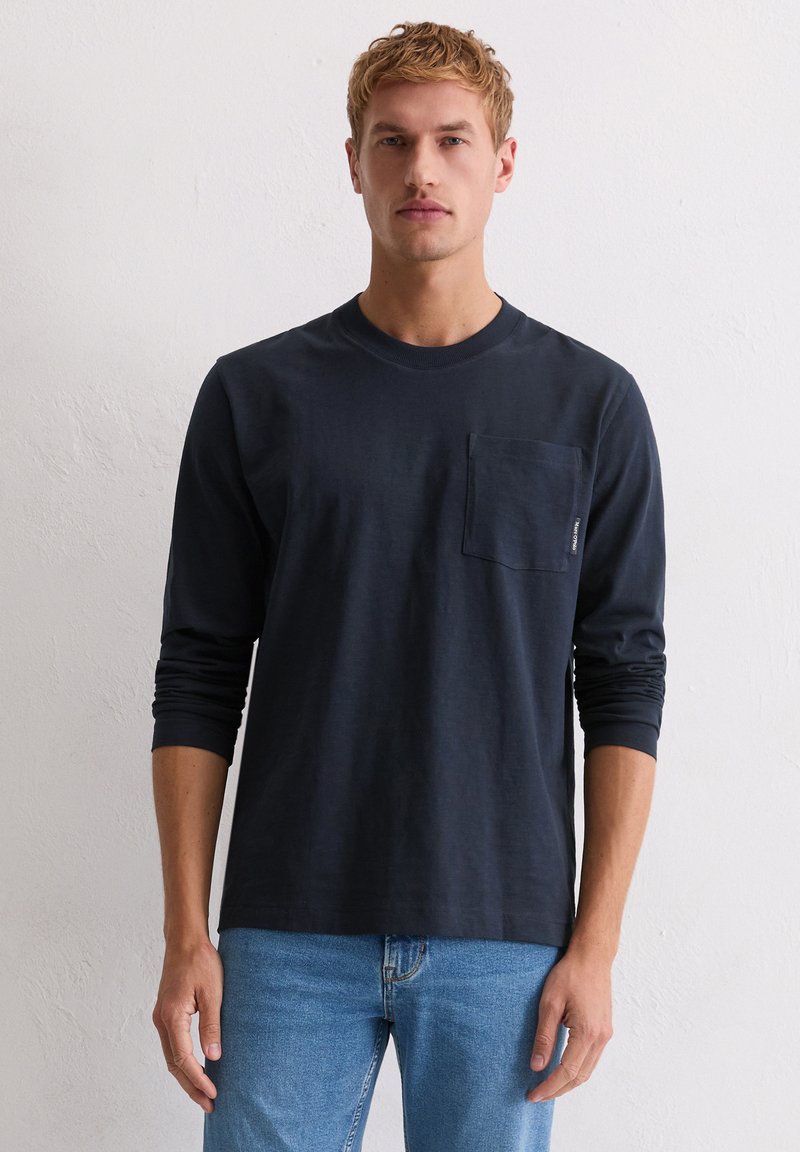 Granatowa koszulka z długim rękawem wykonana z bawełny, z okrągłym dekoltem i kieszonką na piersi. Tkanina wydaje się gładka, a krój casualowy.