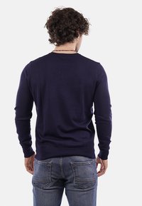 Pullover a maniche lunghe blu navy, orlo e polsini a coste, scollatura rotonda, silhouette aderente, texture morbida, abbinato a jeans blu.