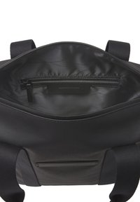 Intérieur d'un sac textile noir avec une doublure lisse, une poche zippée et une étiquette visible. Design minimaliste avec des poignées robustes.